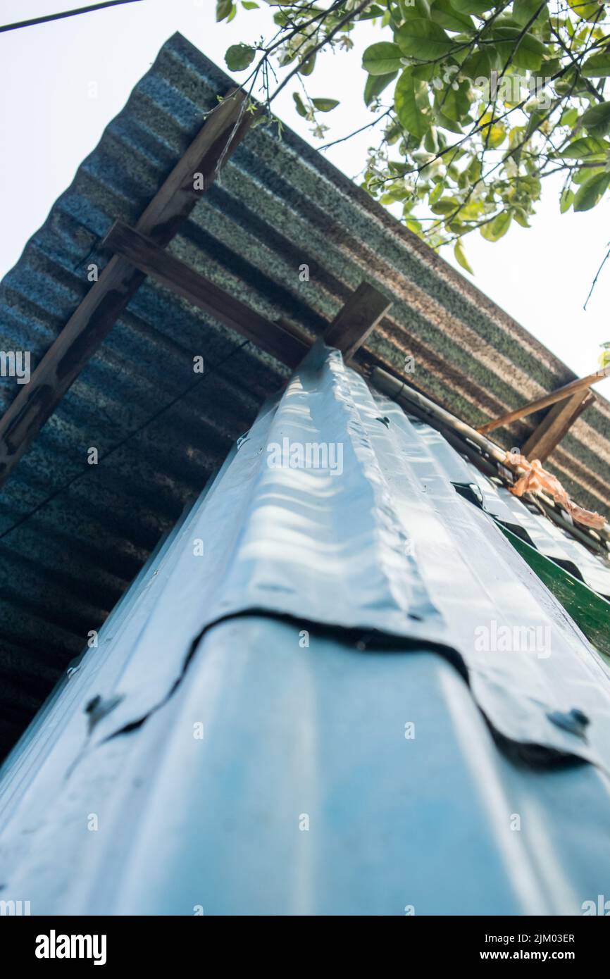 A bottom-up photo of a corner of a village house made of GCI sheets. The roof of the house is also made of GCI sheets. Stock Photo