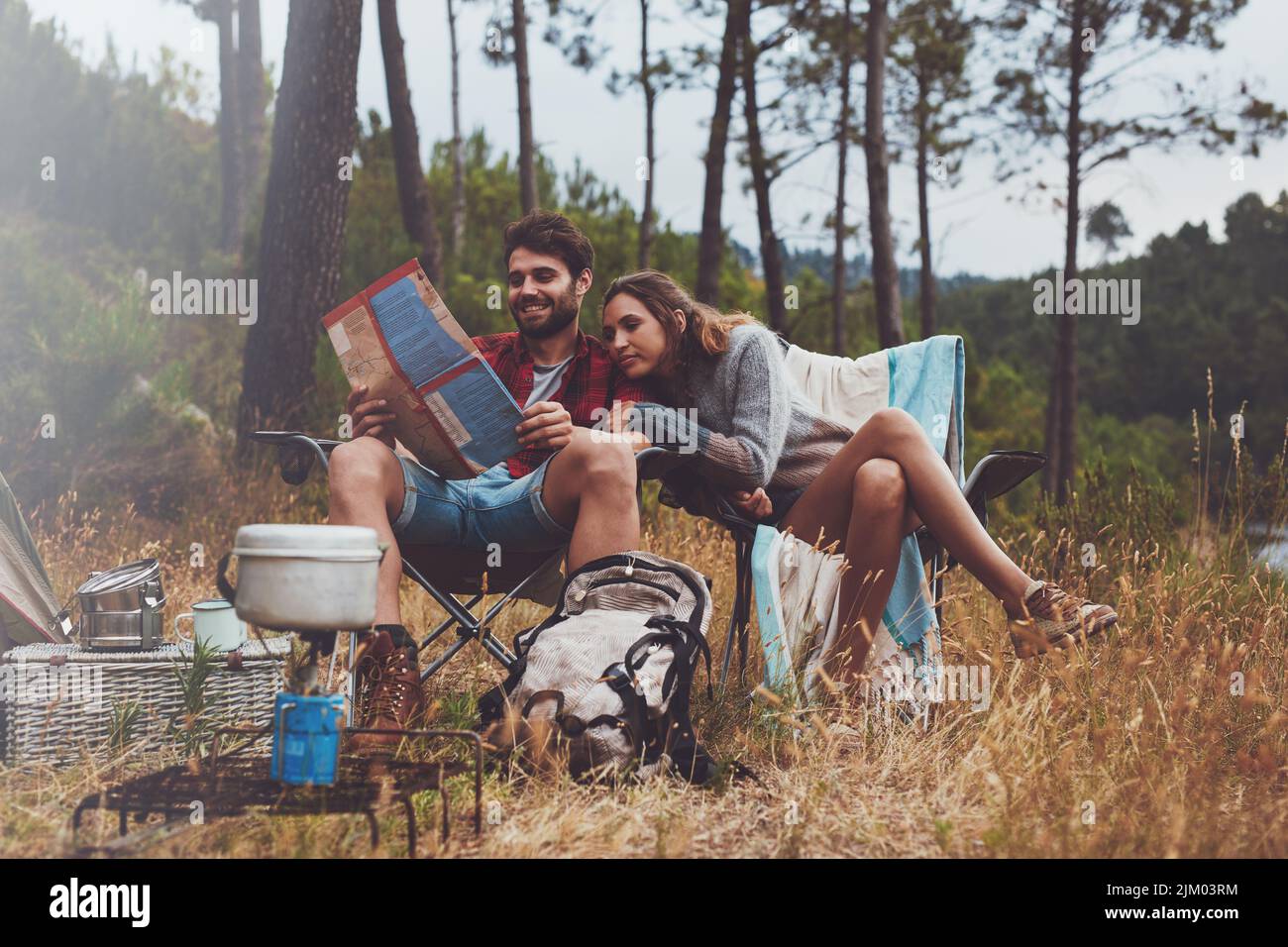 Young man and woman looking at a travel map while sitting at their campsite. Adventurous young couple camping outdoors in nature. Stock Photo