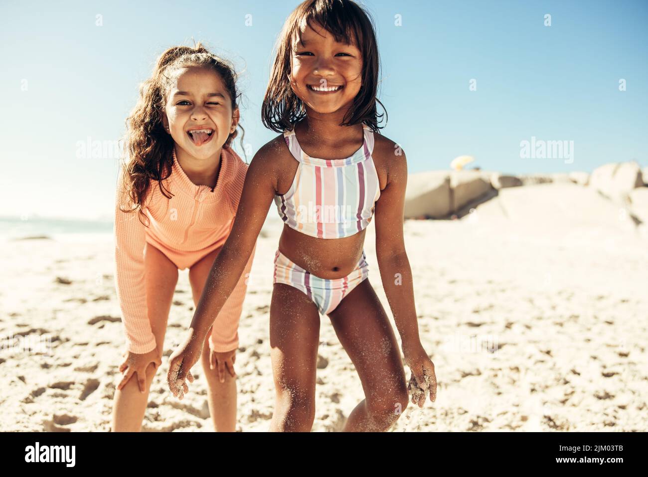 Adorable little girls having fun together at the beach during summer vacation. Two happy young kids smiling at the camera while covered in beach sand. Stock Photo