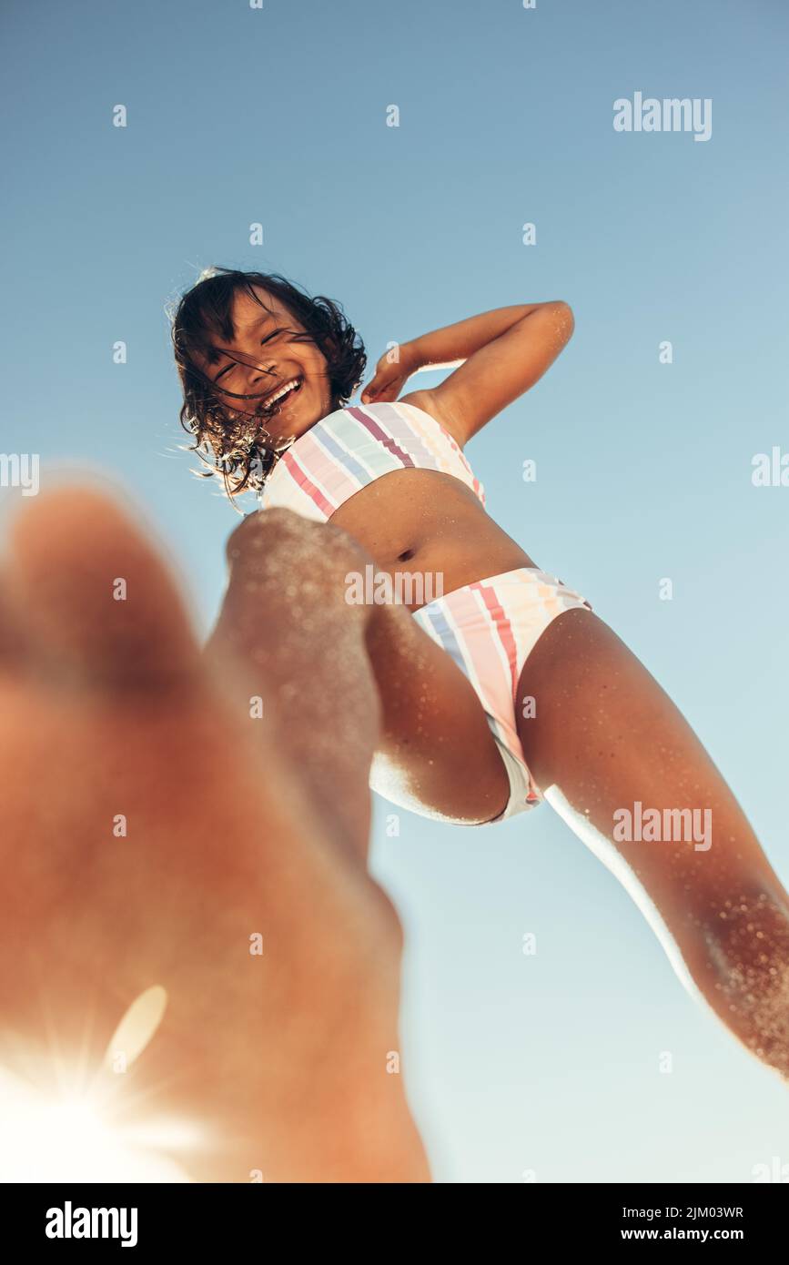 Active young girl playing and having fun while playing on beach sand. Low angle view of an adorable little girl smiling at the camera with the sky in Stock Photo