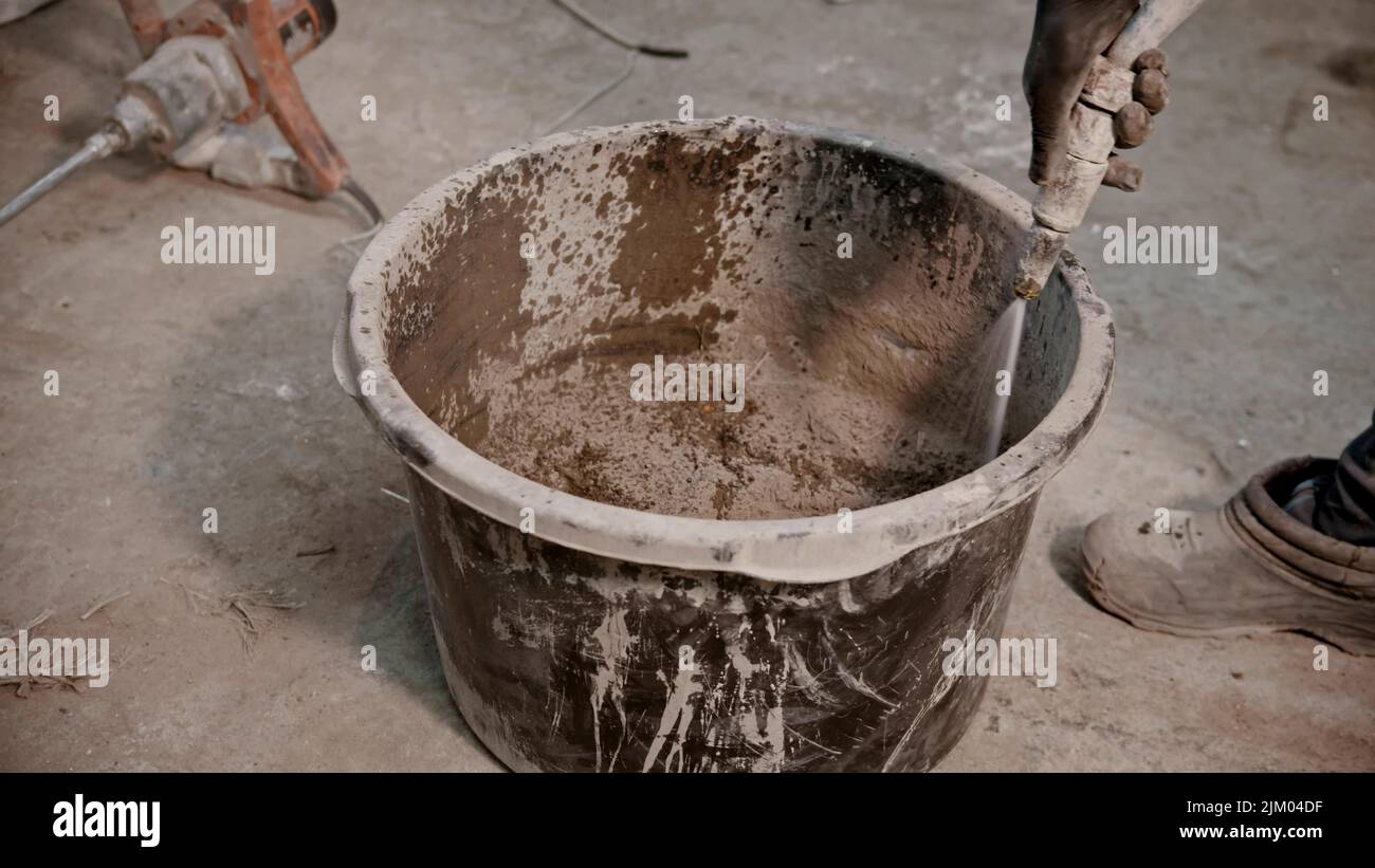 Concrete industry worker adding water in the bucket full of dry