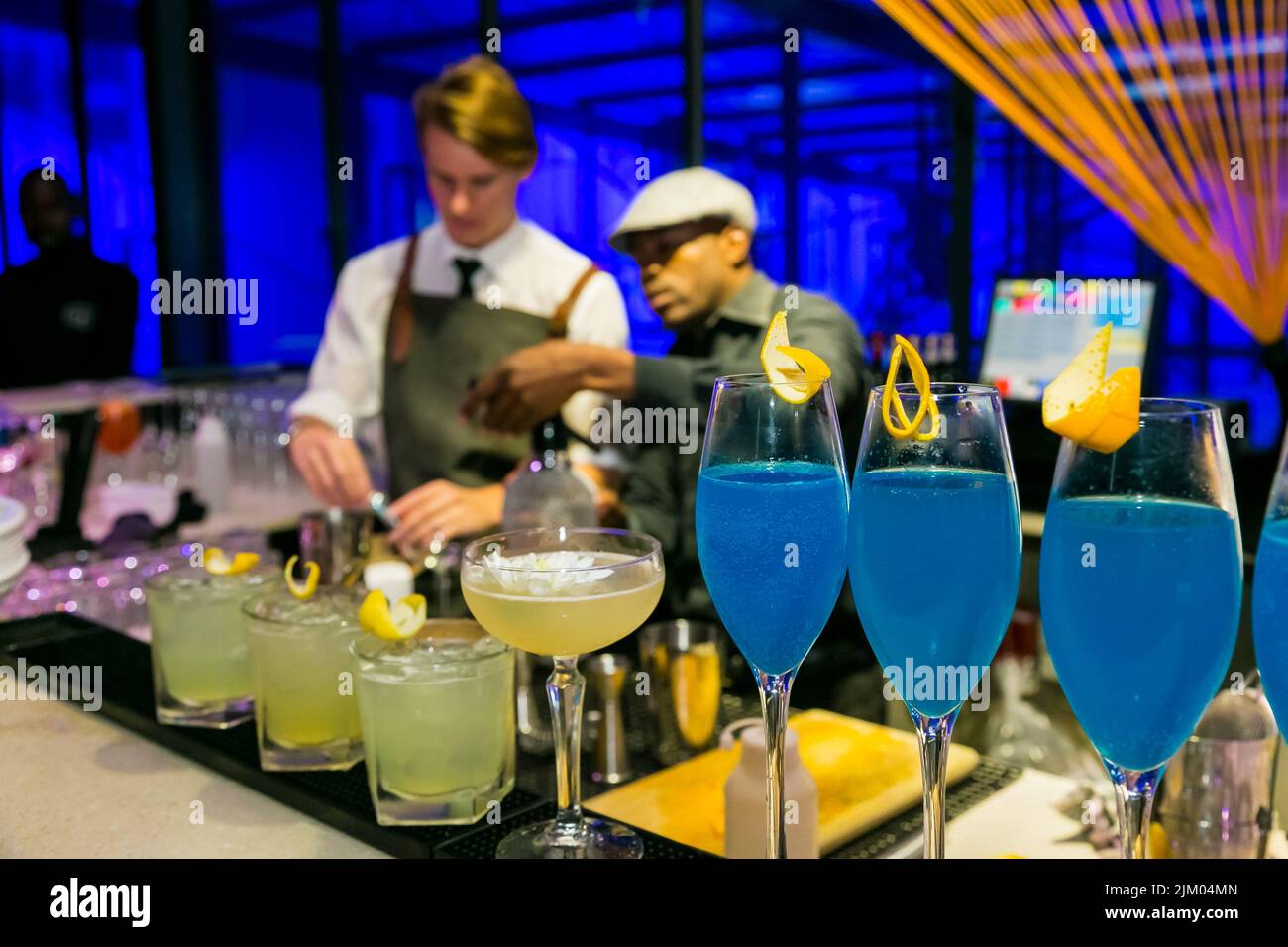 A closeup of a row of glasses with blue and yellow drinks on the bar counter with lemon zest on them Stock Photo