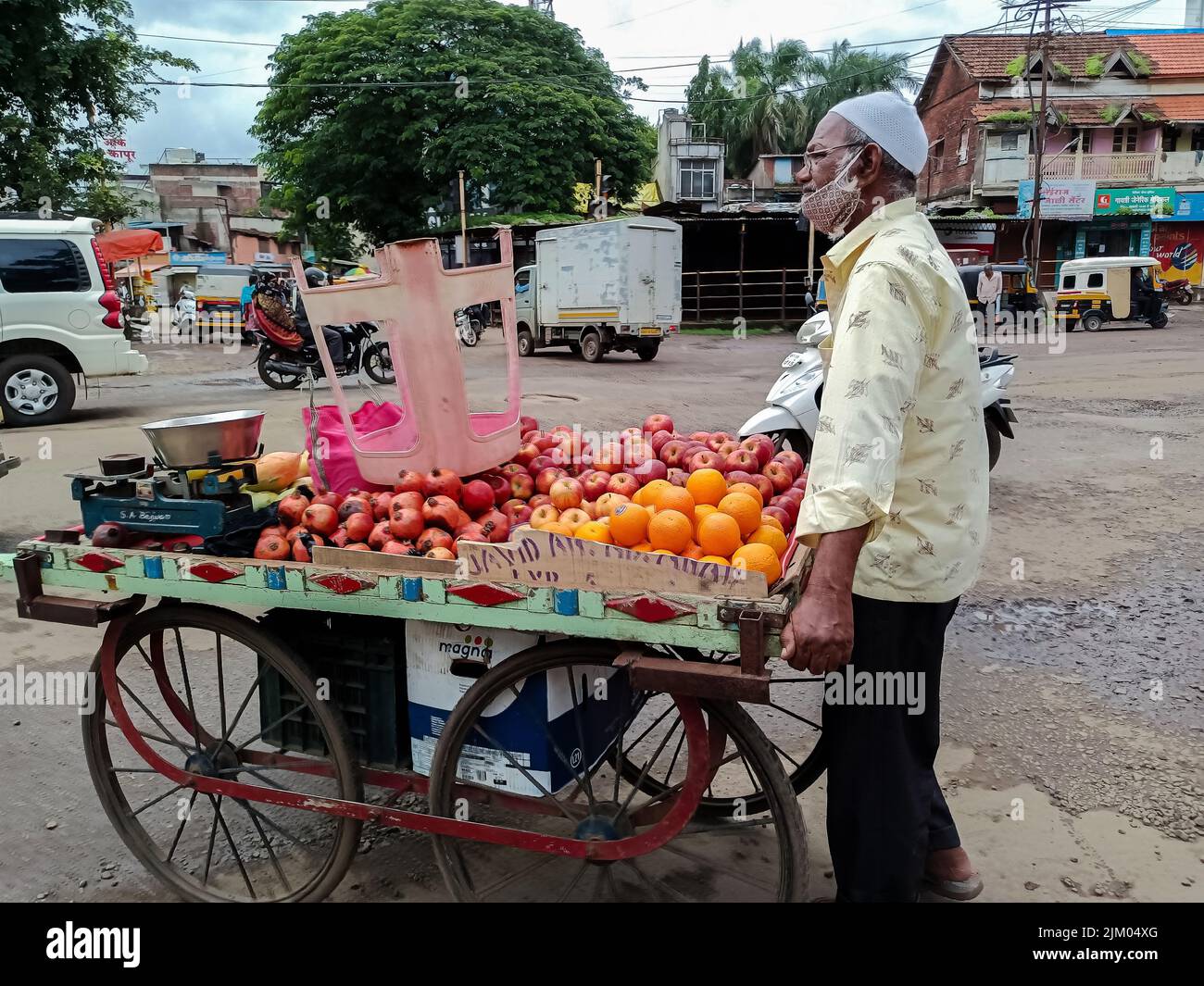 Kolhapur, India- July 16th 2021; Stock photo of 50 to 60 year old Indian fruit seller selling fresh fruits like apple , orange etc on wooden cart in c Stock Photo
