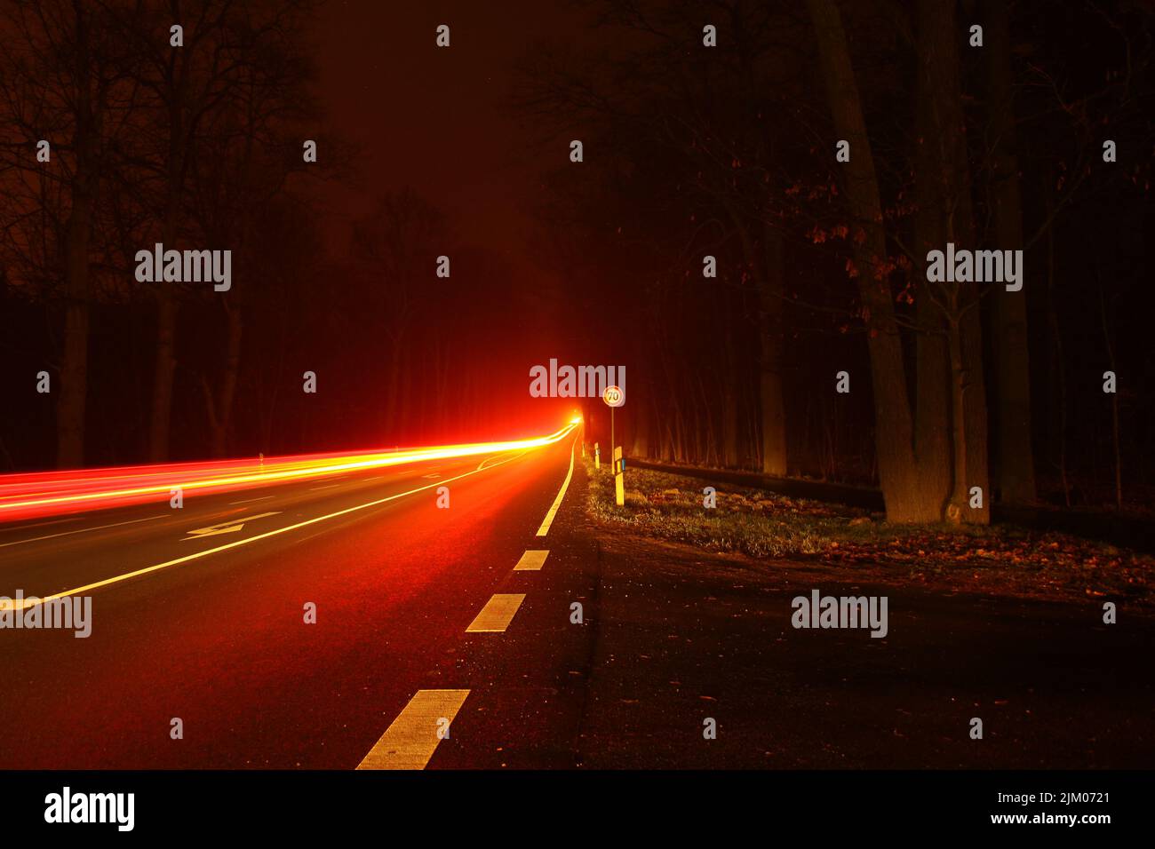 The long exposure of red lights on a highway in the forest in the evening Stock Photo