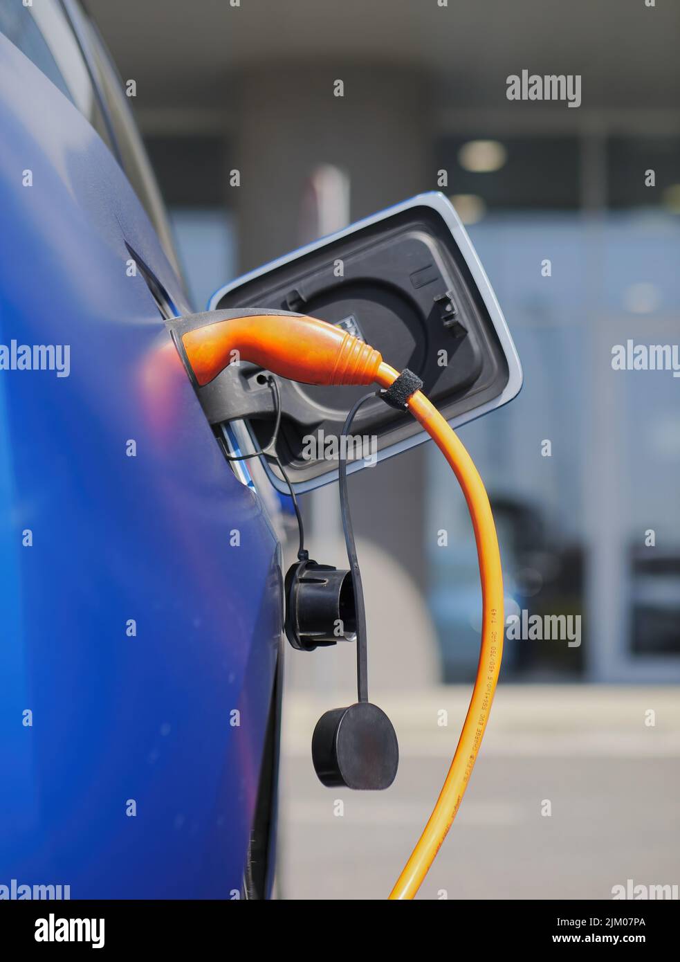 A vertical closeup shot of an electric car being charged with an orange charger Stock Photo