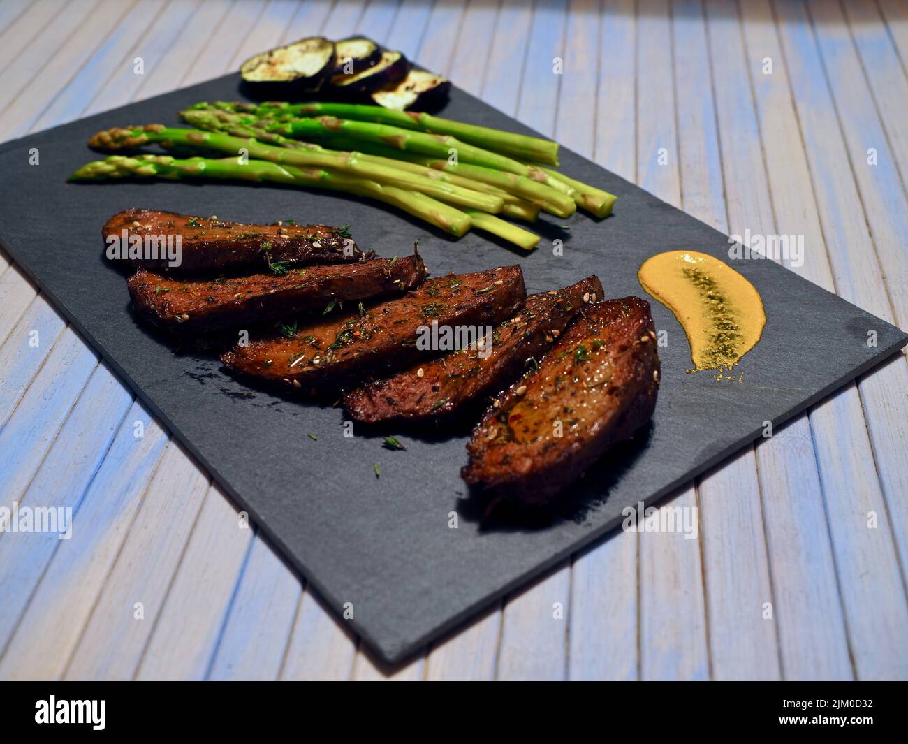 close up view of a sliced vegan meat, served with asparagus and grilled aubergines and a yellow sauce Stock Photo