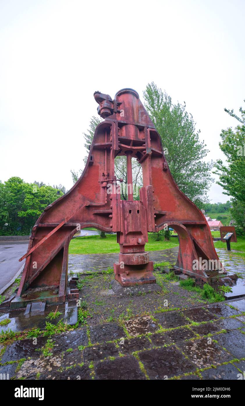A large metal, steel steam hammer, painted orange, red, next to the museum parking lot entrance. At the Blaenavon Ironworks Museum in Blaenavon, Wales Stock Photo