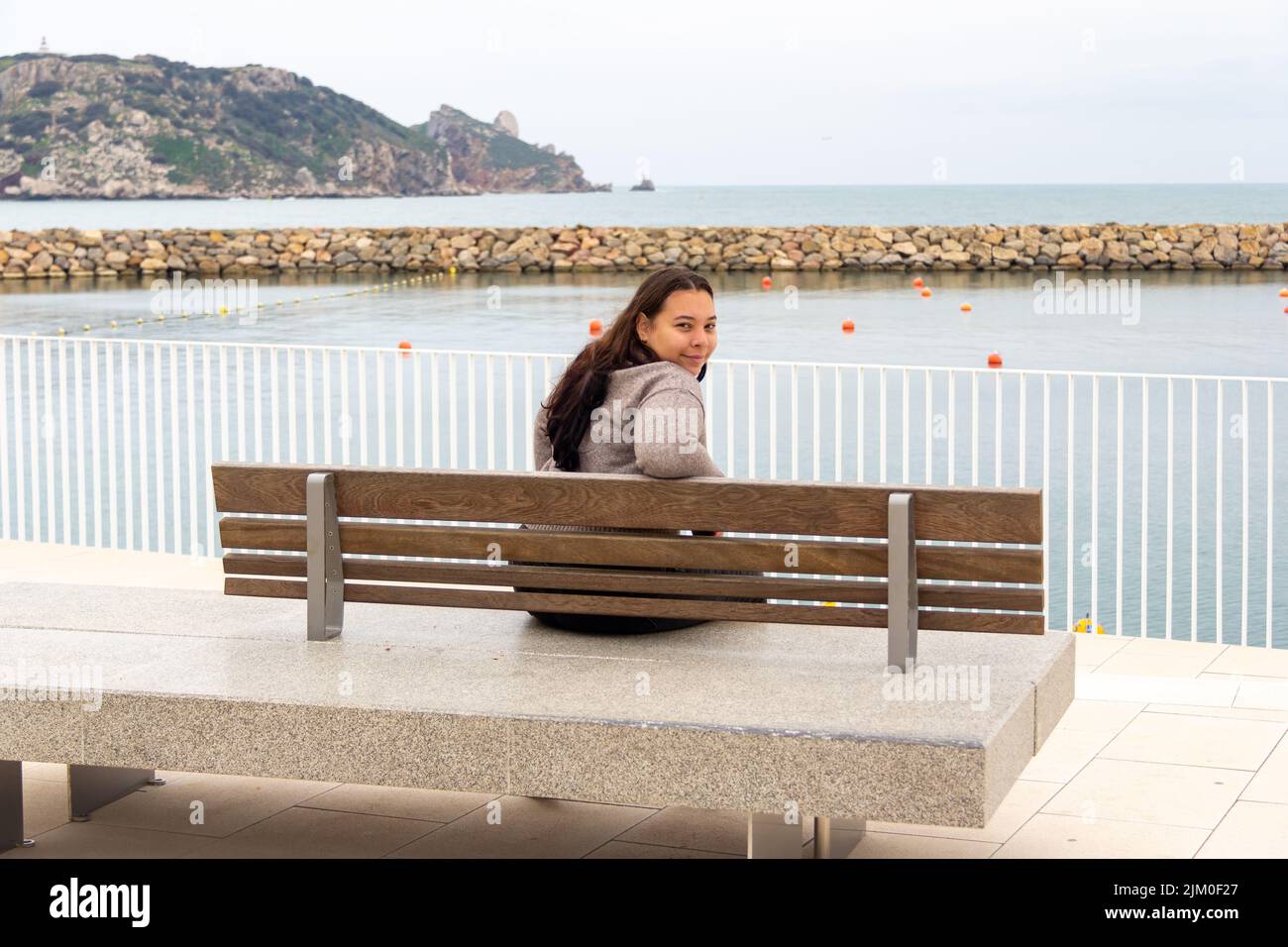 young girl looking back, seated on seaport lookout point Stock Photo