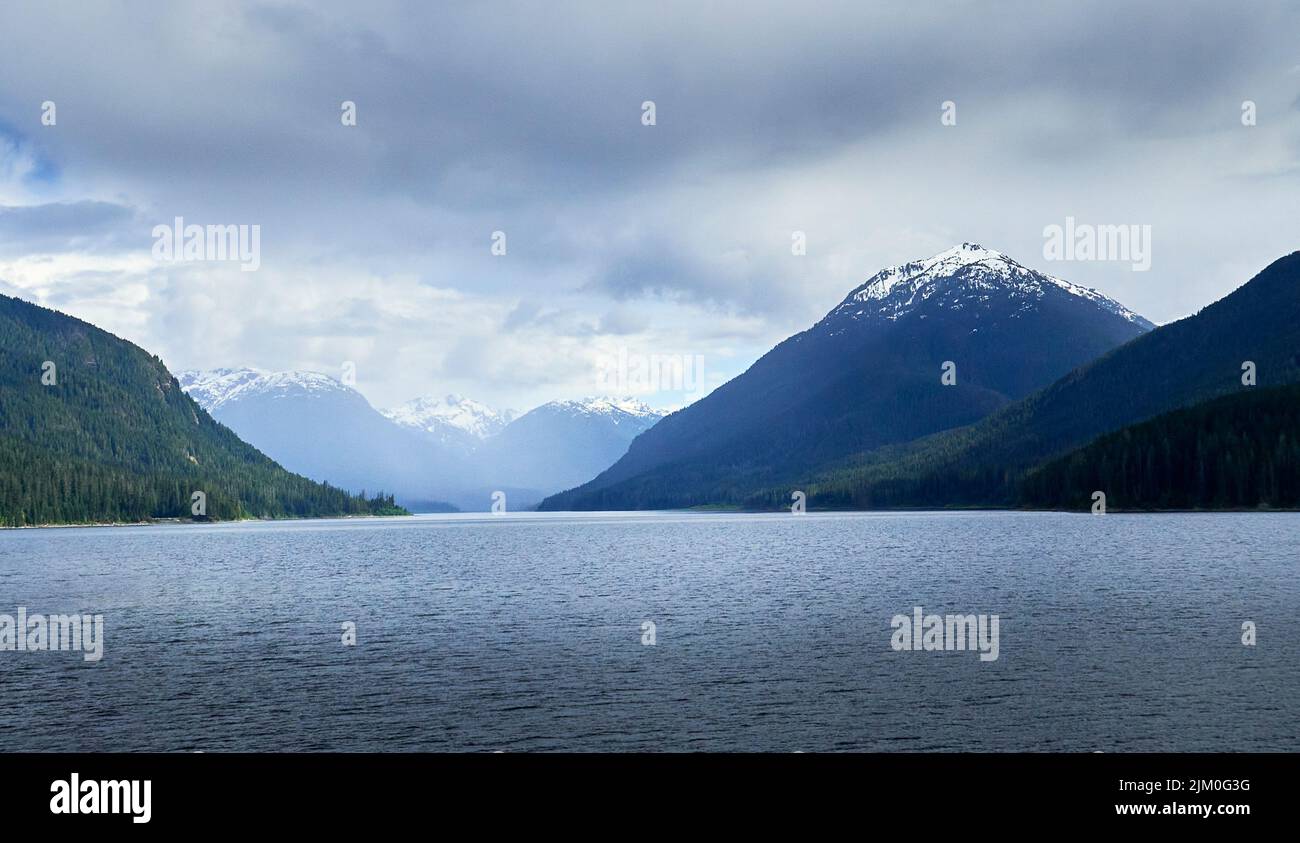 Distant rugged snow covered mountain tops on an overcast day with a serene lake in the forground. Stock Photo