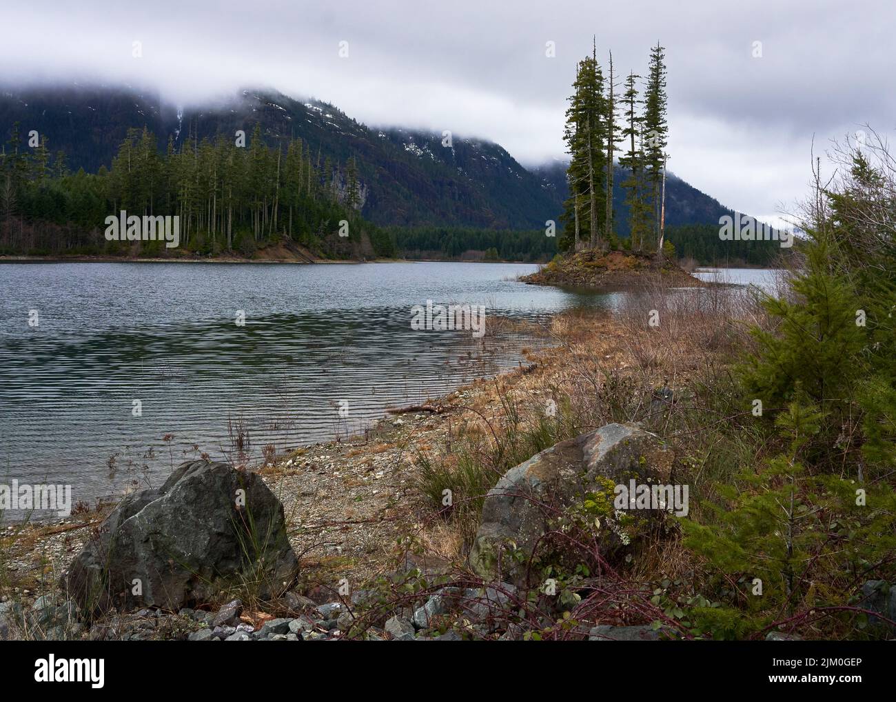 View of a alke and the distant forest covered mountains on an overcast day. Stock Photo