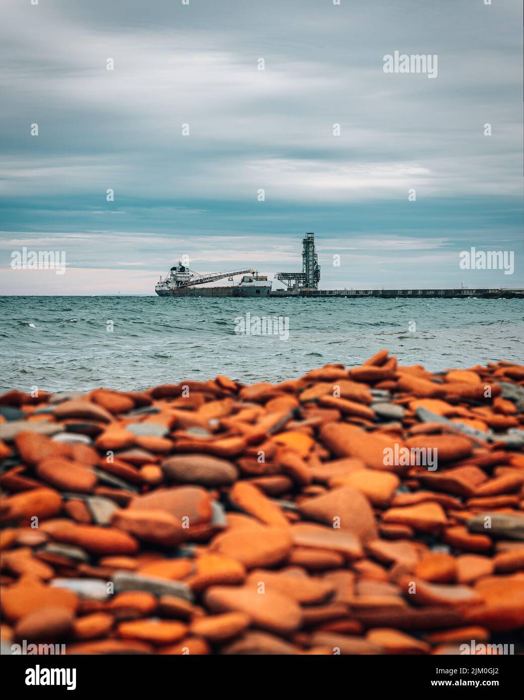 A vertical shot of pebbles on a beach with a ship in the background Stock Photo