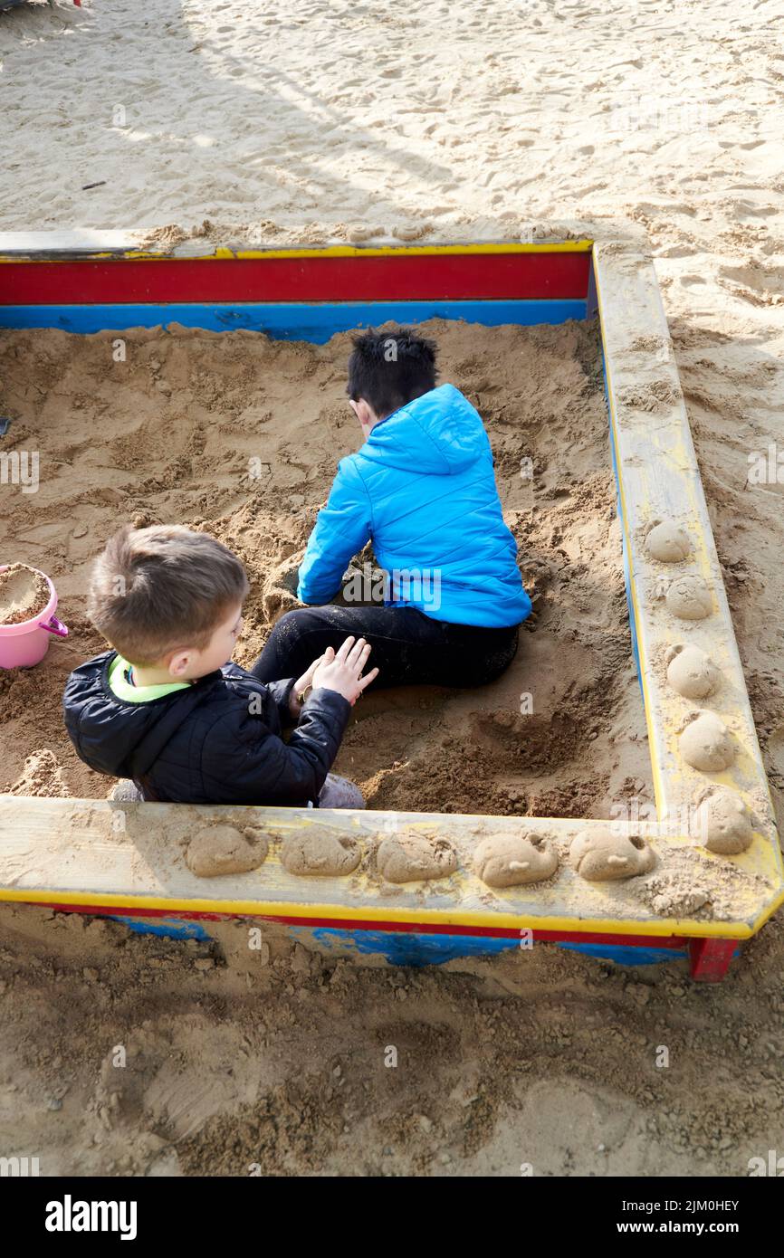 A view of two young boys playing with plastic toys in a sandpit at a playground Stock Photo