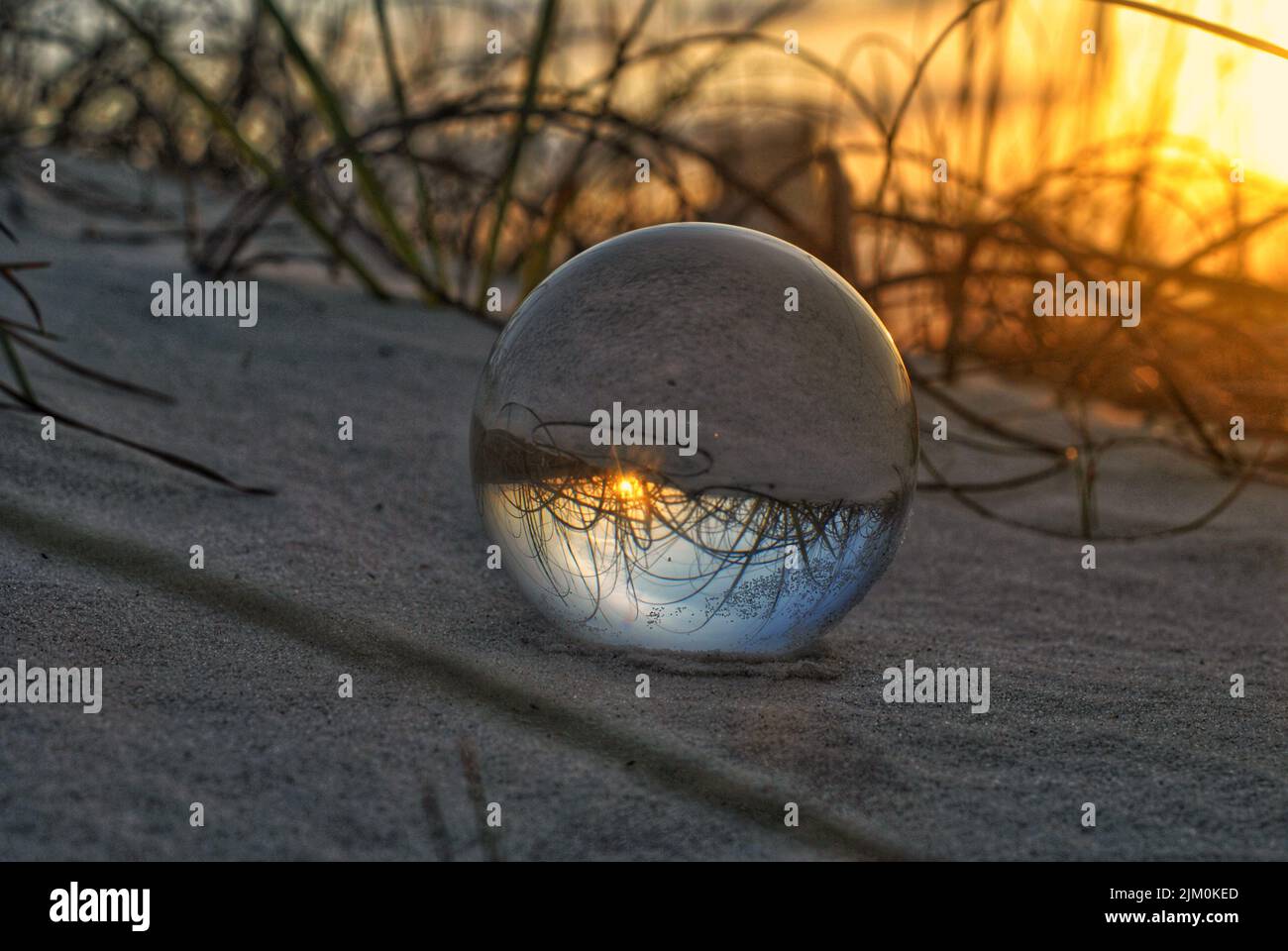 A closeup shot of a glass ball on sand reflecting the beautiful view of the sunset Stock Photo