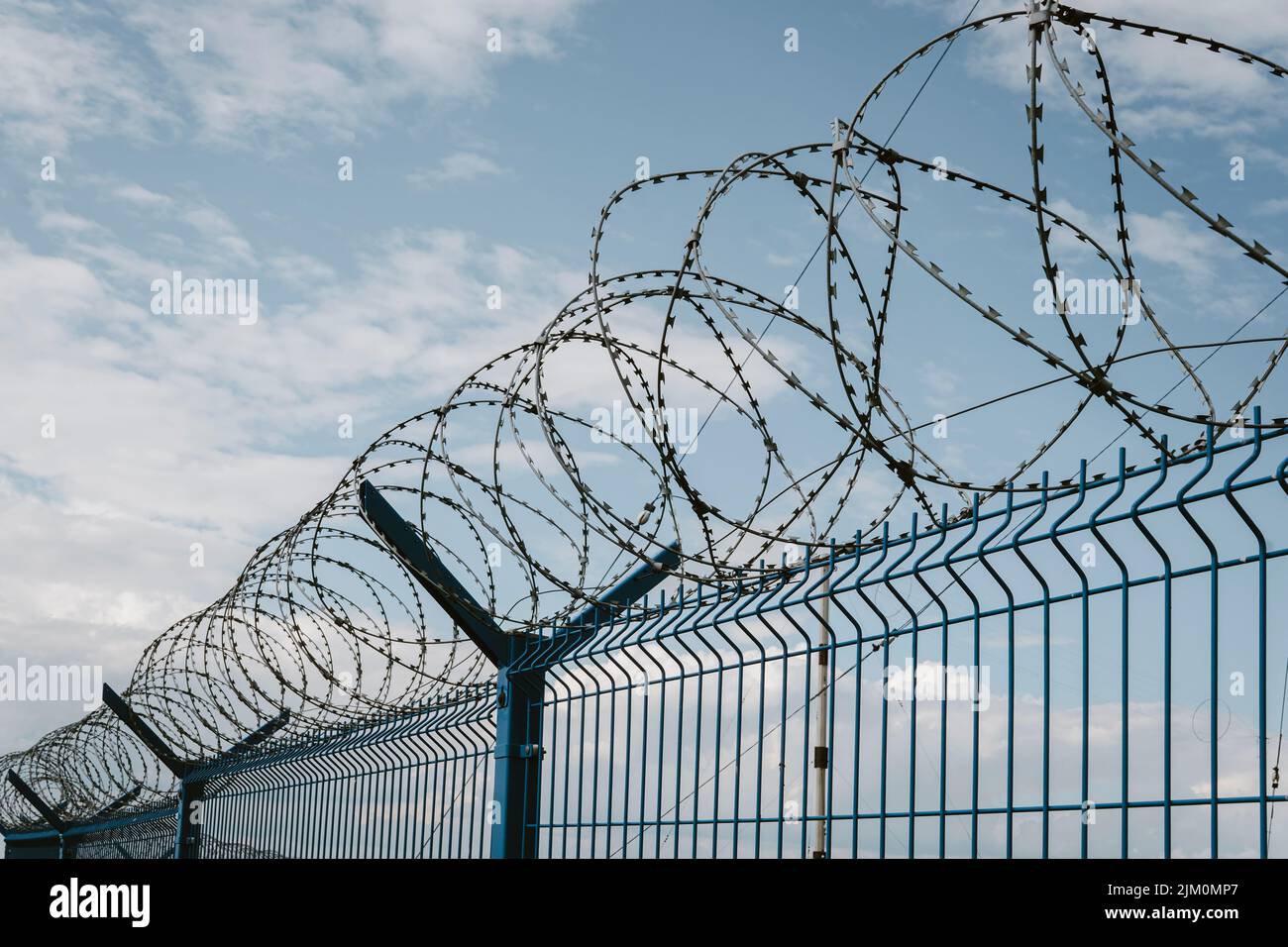 Coiled barbed wire fencing against a blue sky background Stock Photo