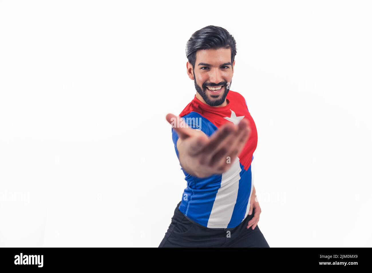 Hispanic man with dark hair and beard wide smile looking into camera wearing puero rico flag t-shirt extended arm inviting to dance. Studio shot. Isolated copy space. High quality photo Stock Photo