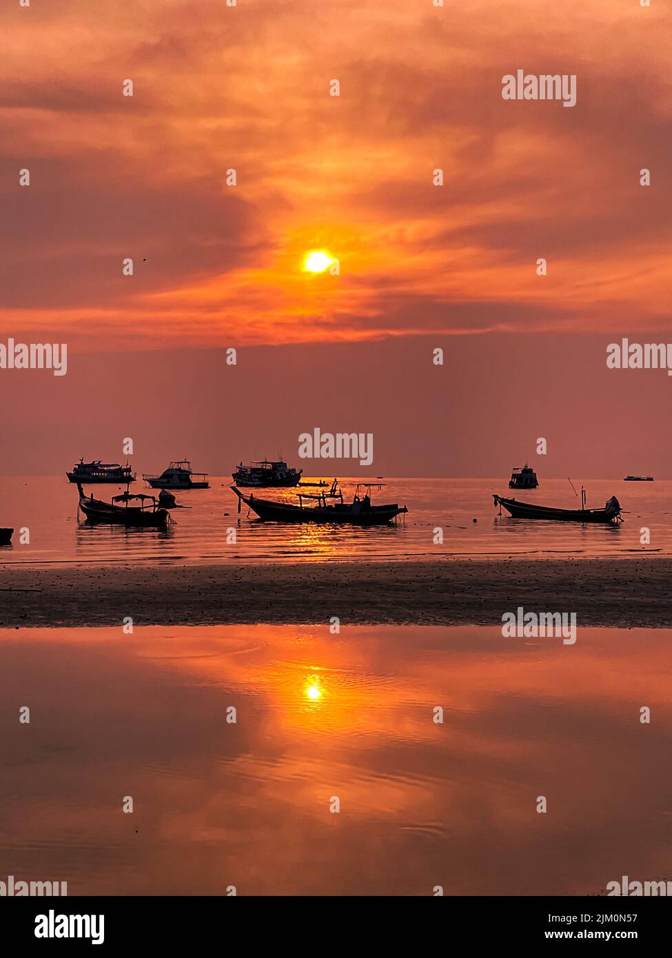 the vertical shot of fishing boats silhouette on a sea water at orange ...