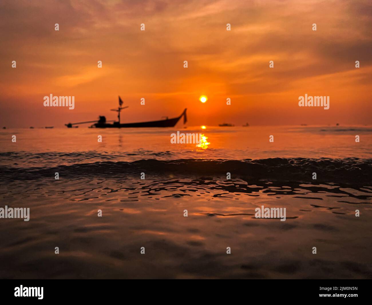 the vertical shot of fishing boats silhouette on seawater at orange ...