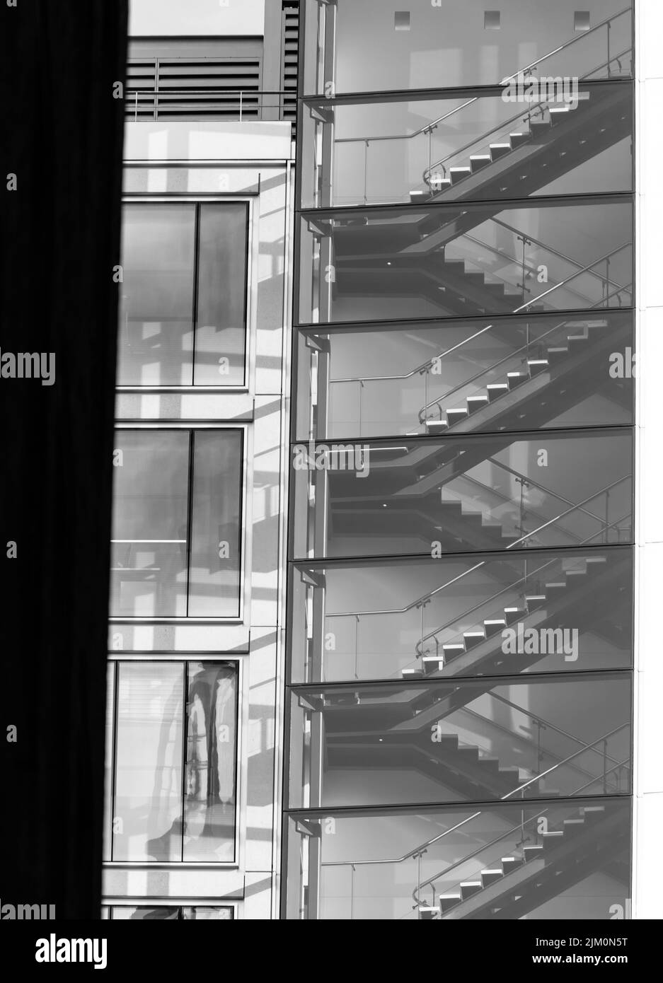 A grayscale vertical shot of emergency stairs in a modern building with glass windows Stock Photo