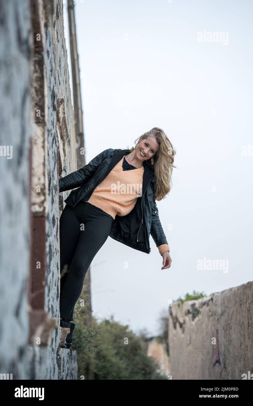 A vertical shot of a Caucasian woman hanging from a wall, smiling Stock Photo