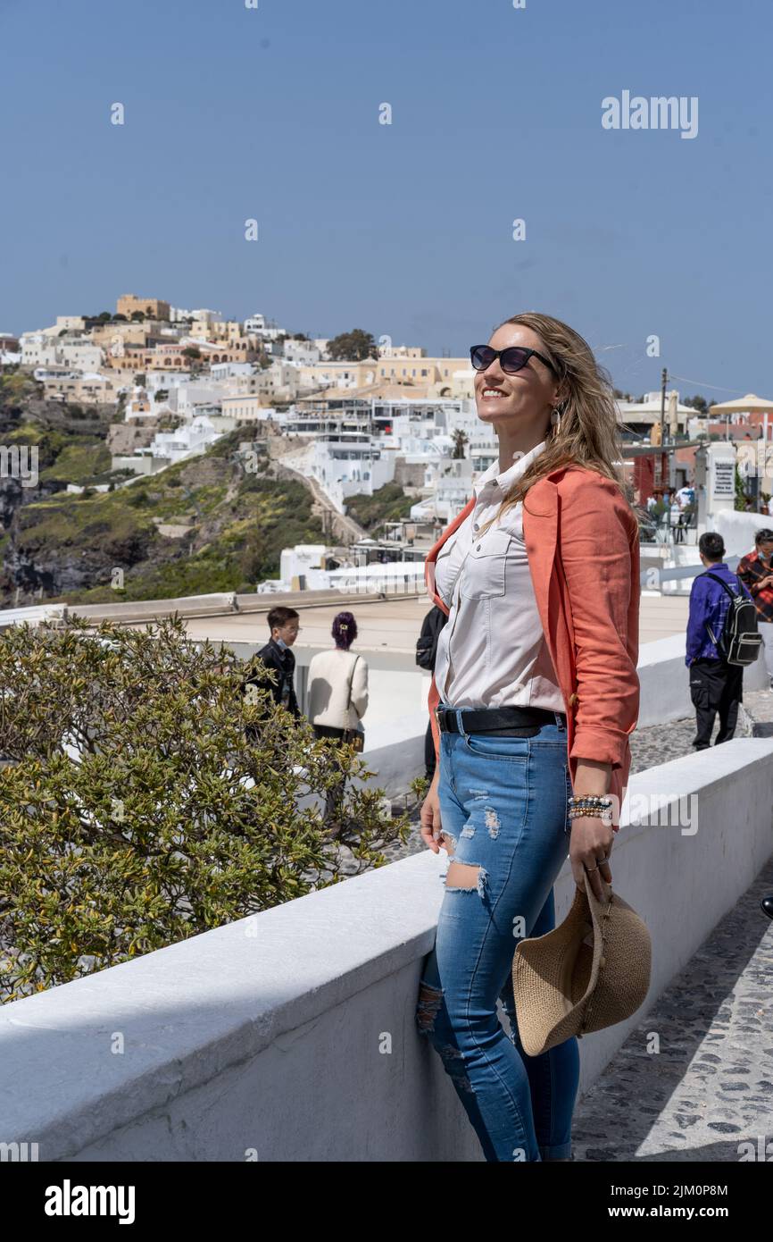 A shallow focus shot of a beautiful Caucasian woman, wearing stylish clothes, over a background of the unique architecture of Santorini, Greece Stock Photo