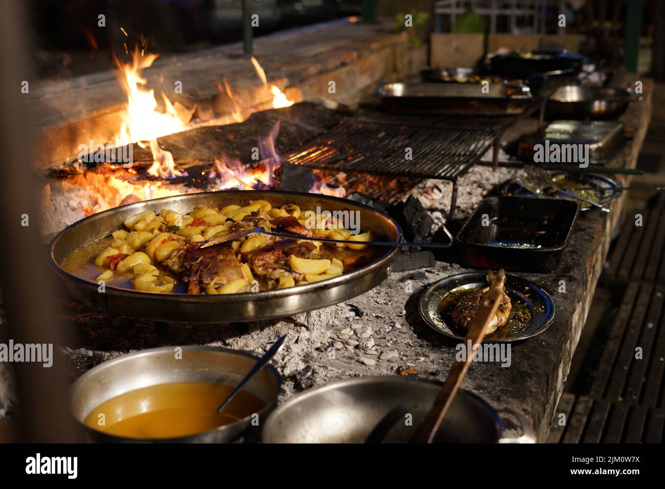 A barbecue grill with flames, potatoes, meats, and sauces Stock Photo