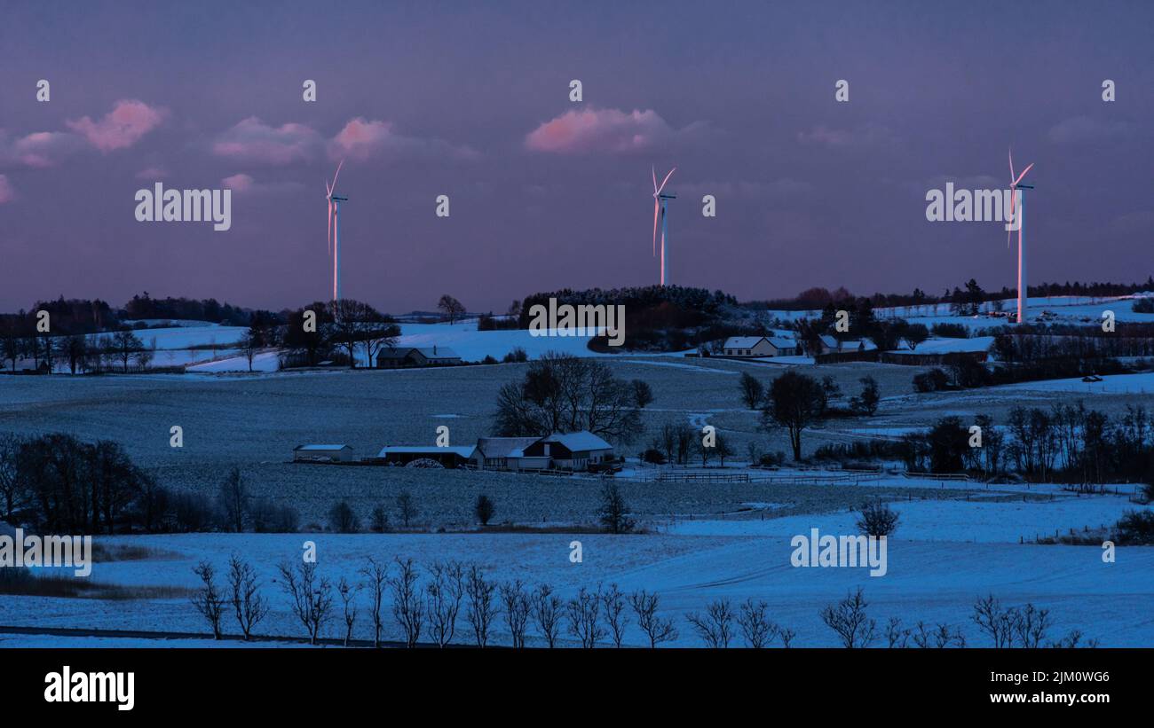 Snow-covered agricultural landscape with three wind turbines illuminated by the first rays of dawn. Assens, Island of Fyn, Denmark, Europe Stock Photo