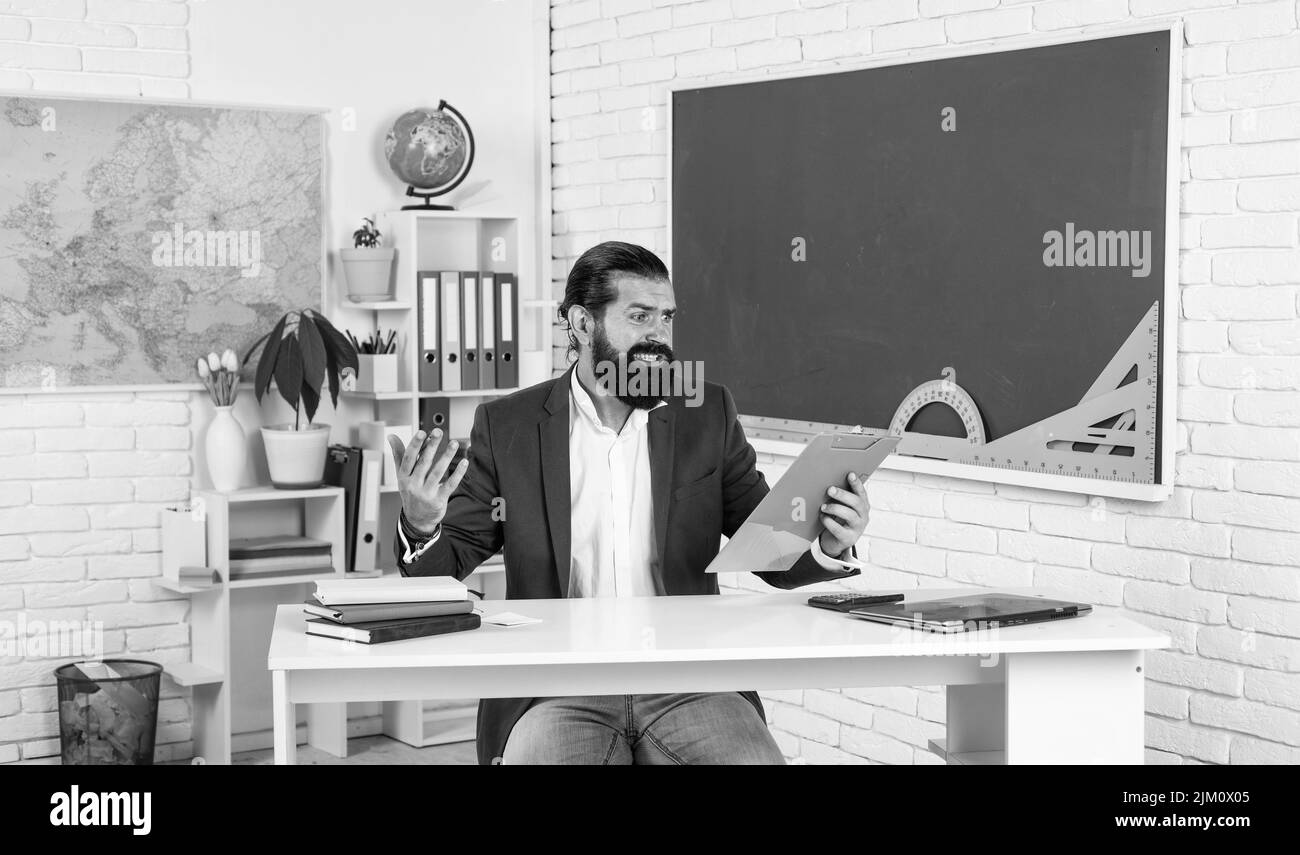 confused man with beard look at notebook. troubles in studying. informal education. male student sit in school classroom while lesson. pass the exam Stock Photo