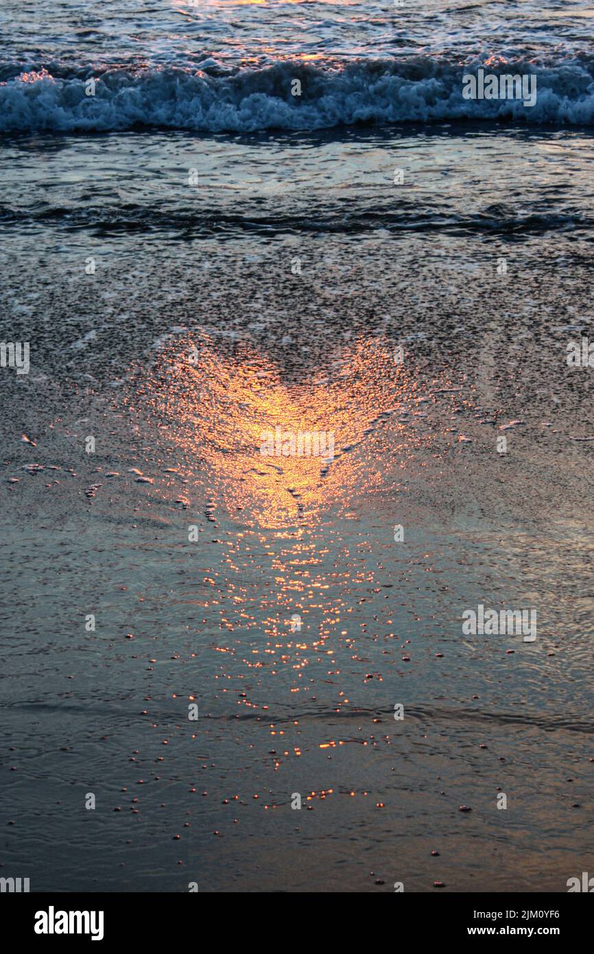 A romantic view of a sandy beach with a heart-shaped reflection of the sunset sun Stock Photo