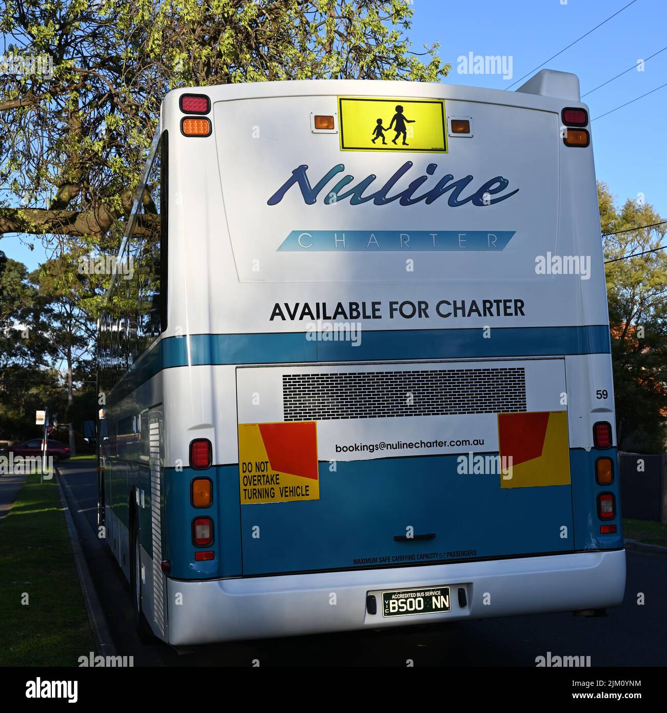 Rear of a predominantly white and blue Nuline charter bus, or coach, in a narrow leafy suburban Melbourne street Stock Photo