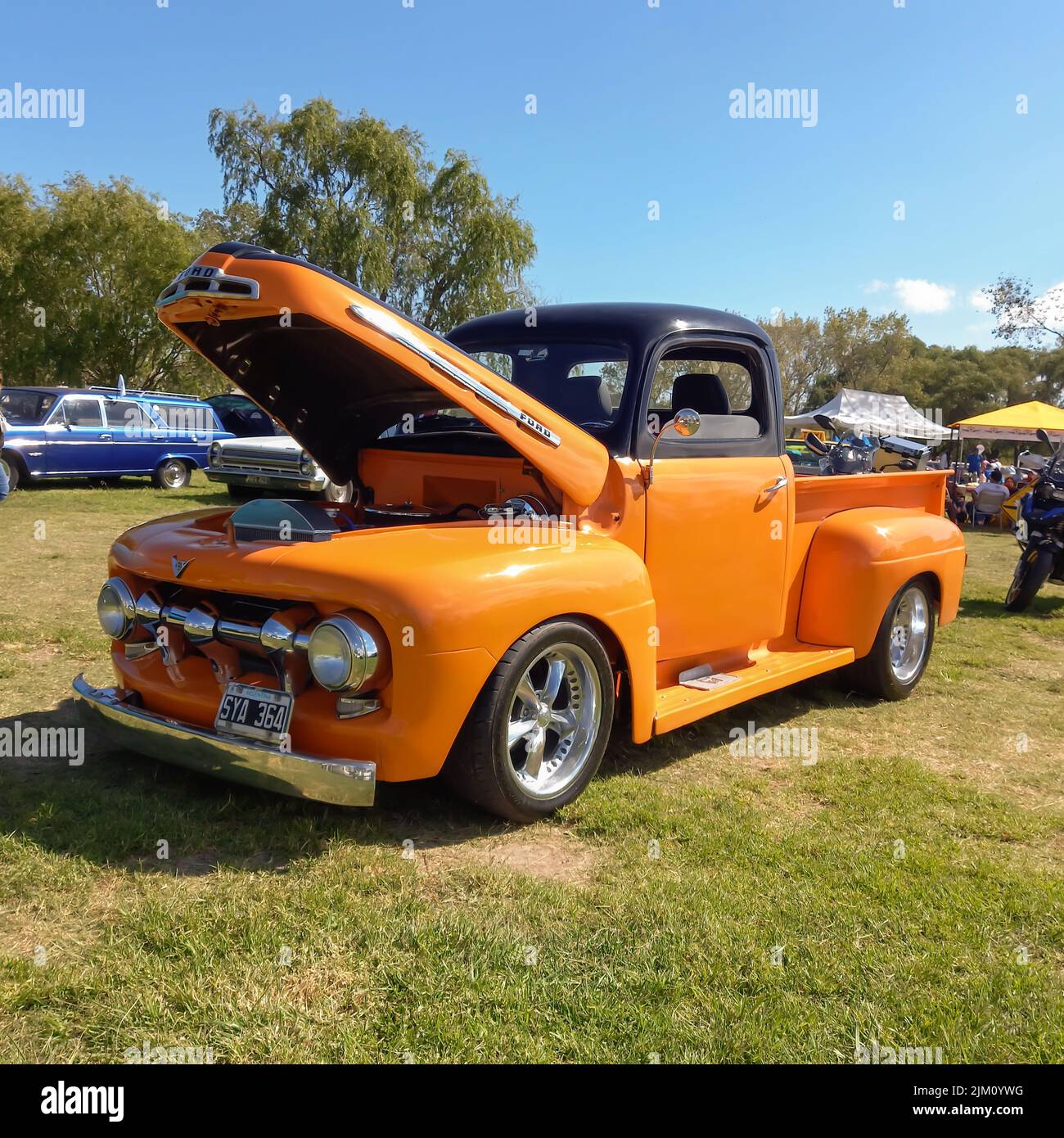 Chascomus, Argentina - Apr 09, 2022: Old orange utility pickup truck Ford F 1 1950s in the countryside. Open hood. Nature grass and trees. Classic car Stock Photo