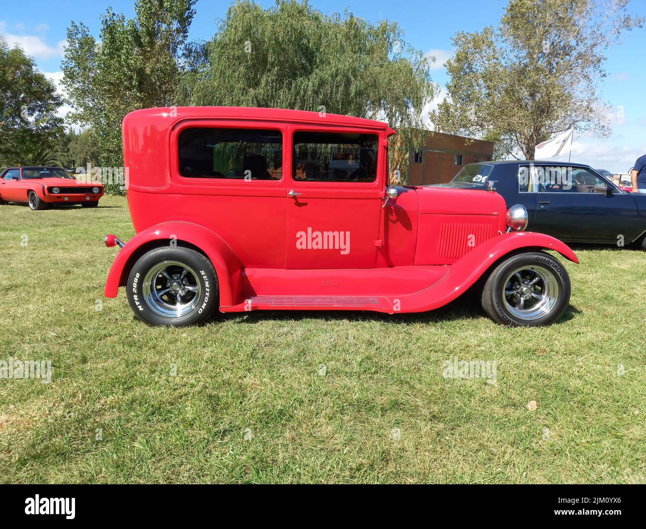 Chascomus, Argentina - Apr 9, 2022: Old red Ford Model A Tudor sedan 1928 - 1931. Hot street rod. Side view. Nature green grass and trees background. Stock Photo