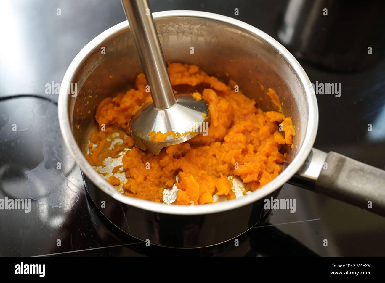 cooked carrots are pureed with a blender in a steel pot on a black