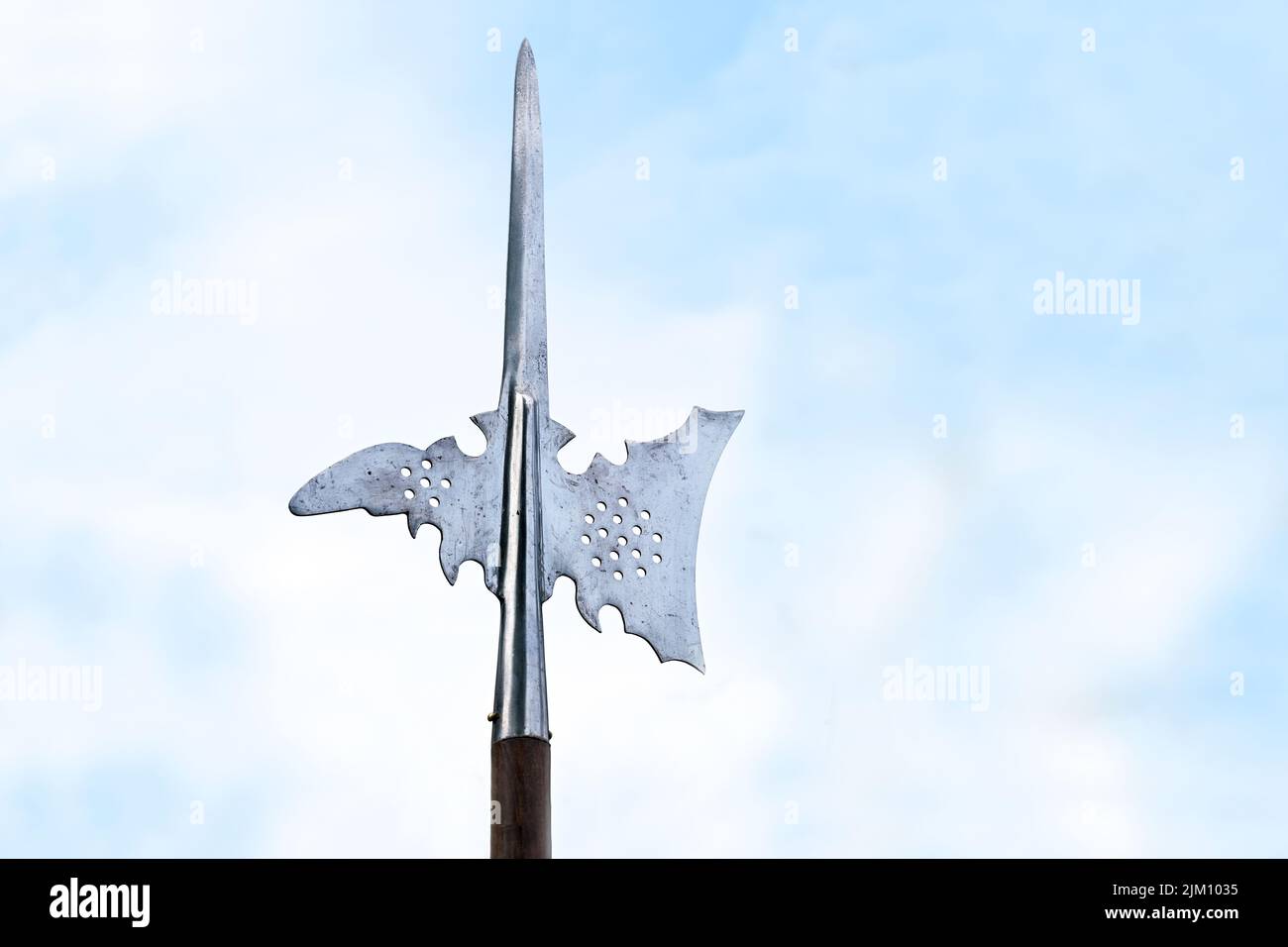 Metal top of a halberd, also called halbard, halbert or Swiss voulge, with axe blade and spike against a cloudy blue sky, pole weapon, copy space, sel Stock Photo