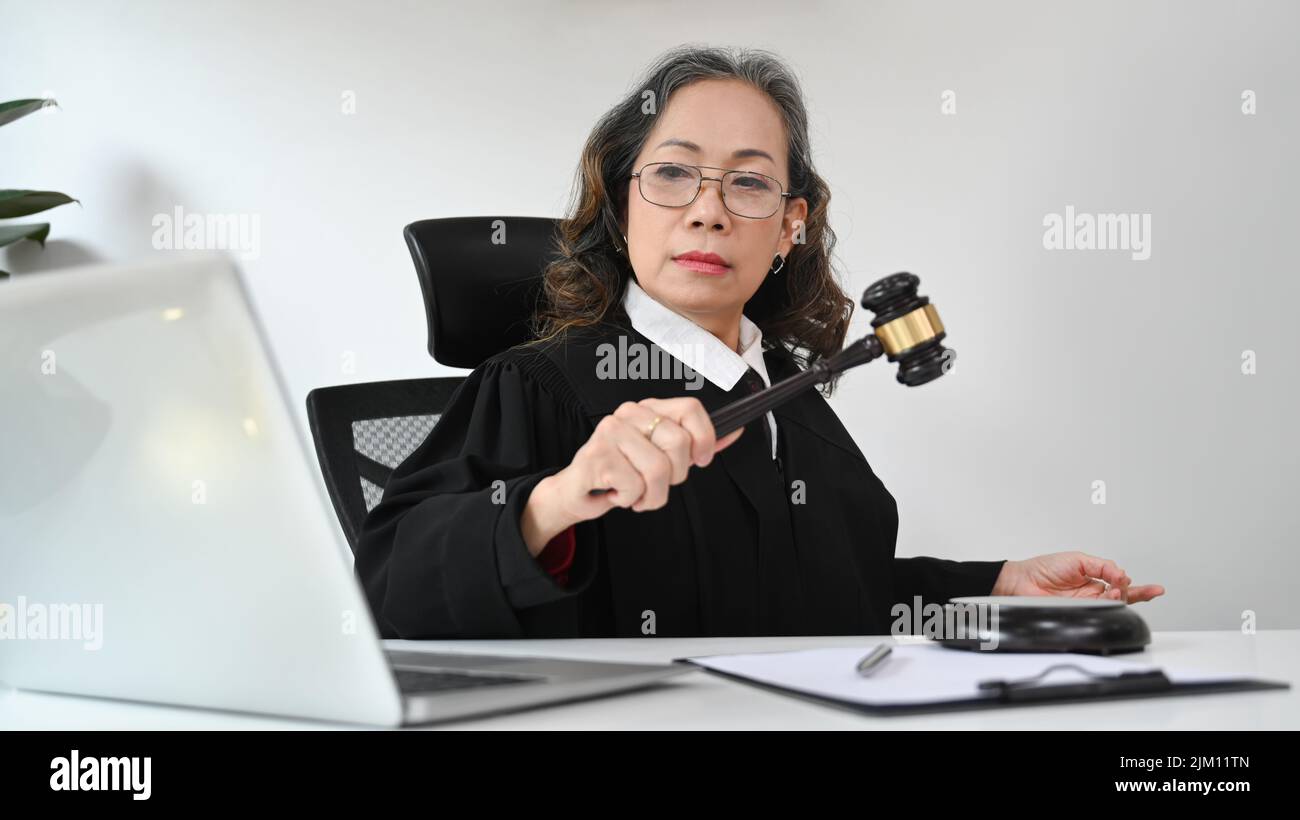 Mature judge or attorney in robe gown uniform consulting online via video conferencing on laptop computer Stock Photo