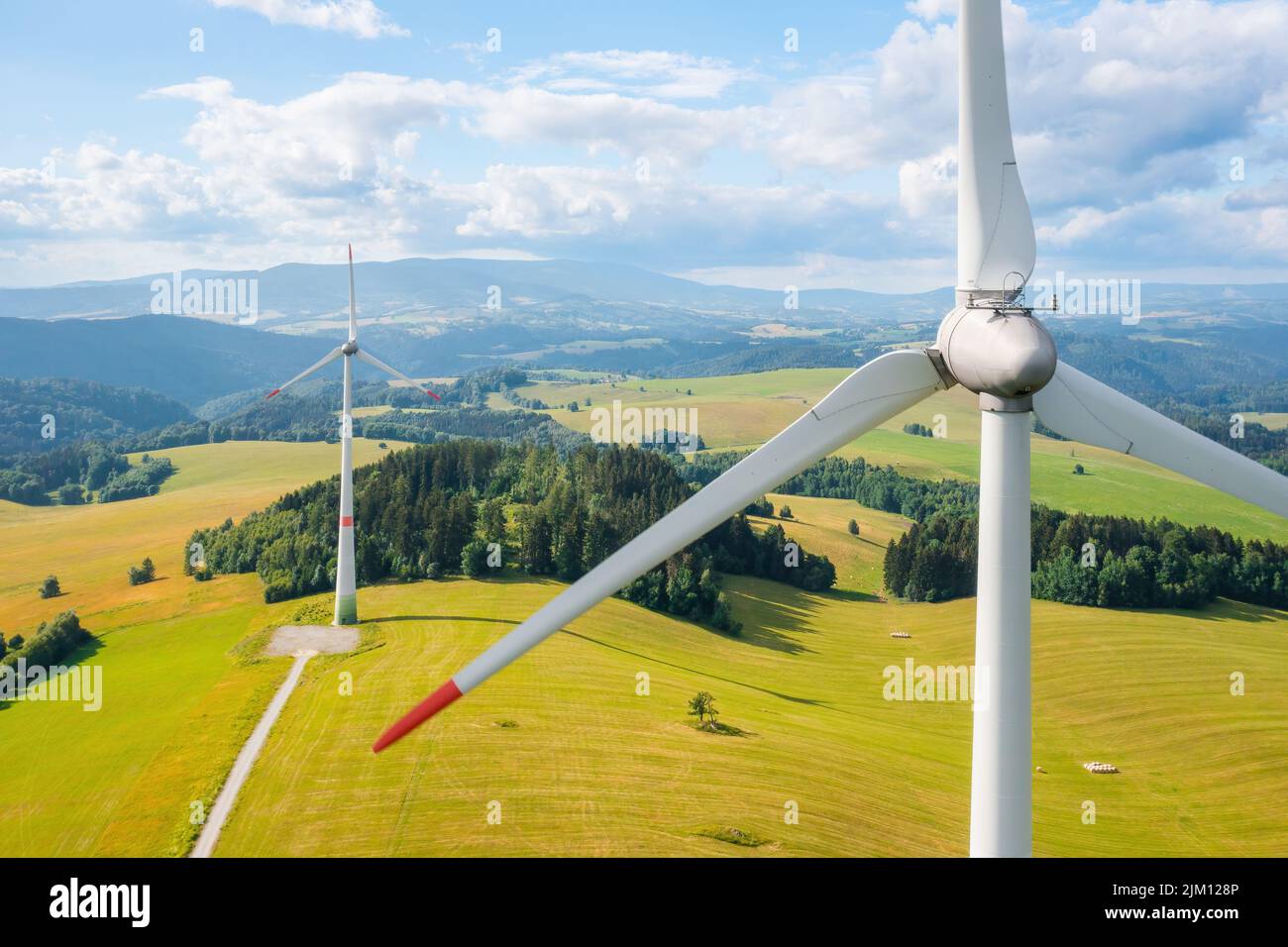 Close up a propeller of a wind turbine in a wind park in the yellow field and mountains in the background in a sunny day. Renewable energy production.  Stock Photo