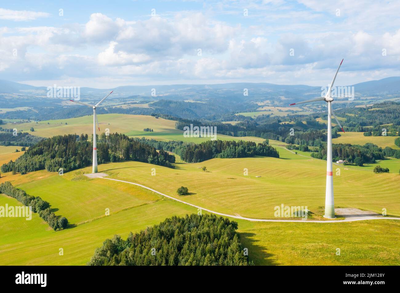 Panoramic view of windmills in the wind farm in the yellow field and mountains on the background. Production of green and renewable energy.  Stock Photo