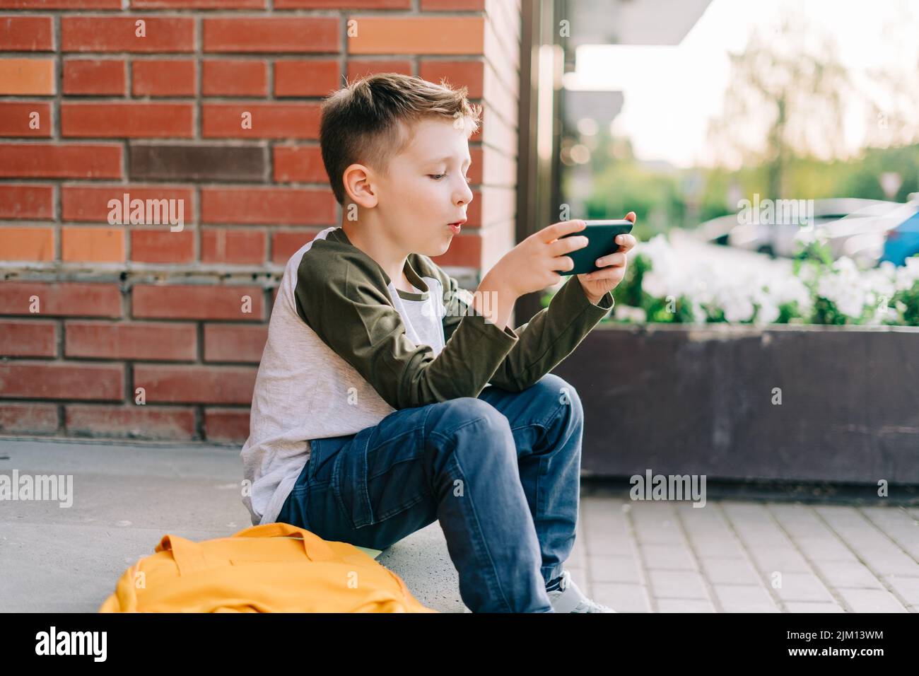 Back to school. Cute child with backpack, holding mobile phone, playing with cellphone. School boy pupil with bag. Elementary school student after Stock Photo