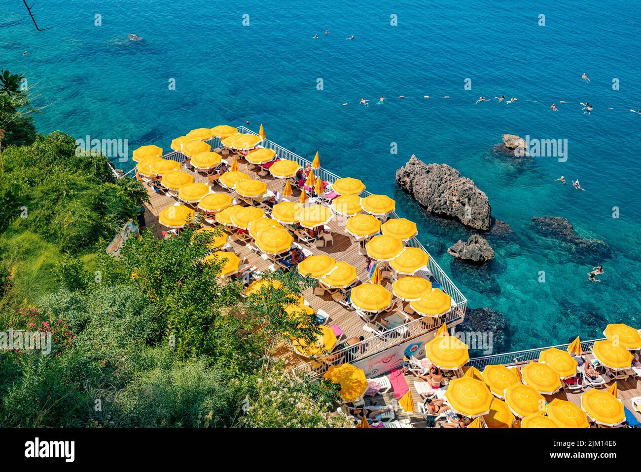 23 June 2022, Antalya, Turkey: Hidden narrow and cozy beach among cliffs and rocks with bright yellow umbrellas and sunbeds and scenic refreshing blue Stock Photo