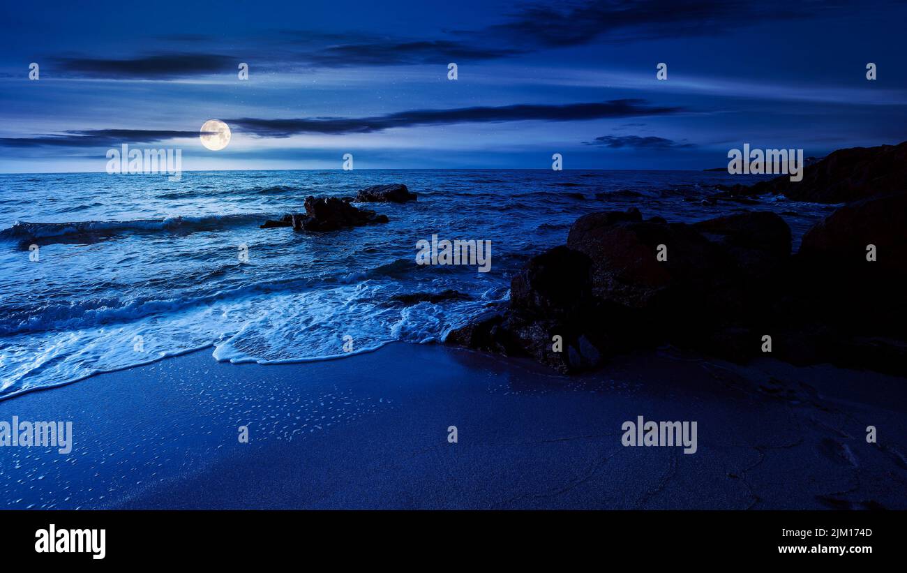 huge stones on the sandy beach at night. wonderful velvet season vacation on the black sea in full moon light. calm waves washing the shore. clouds on Stock Photo