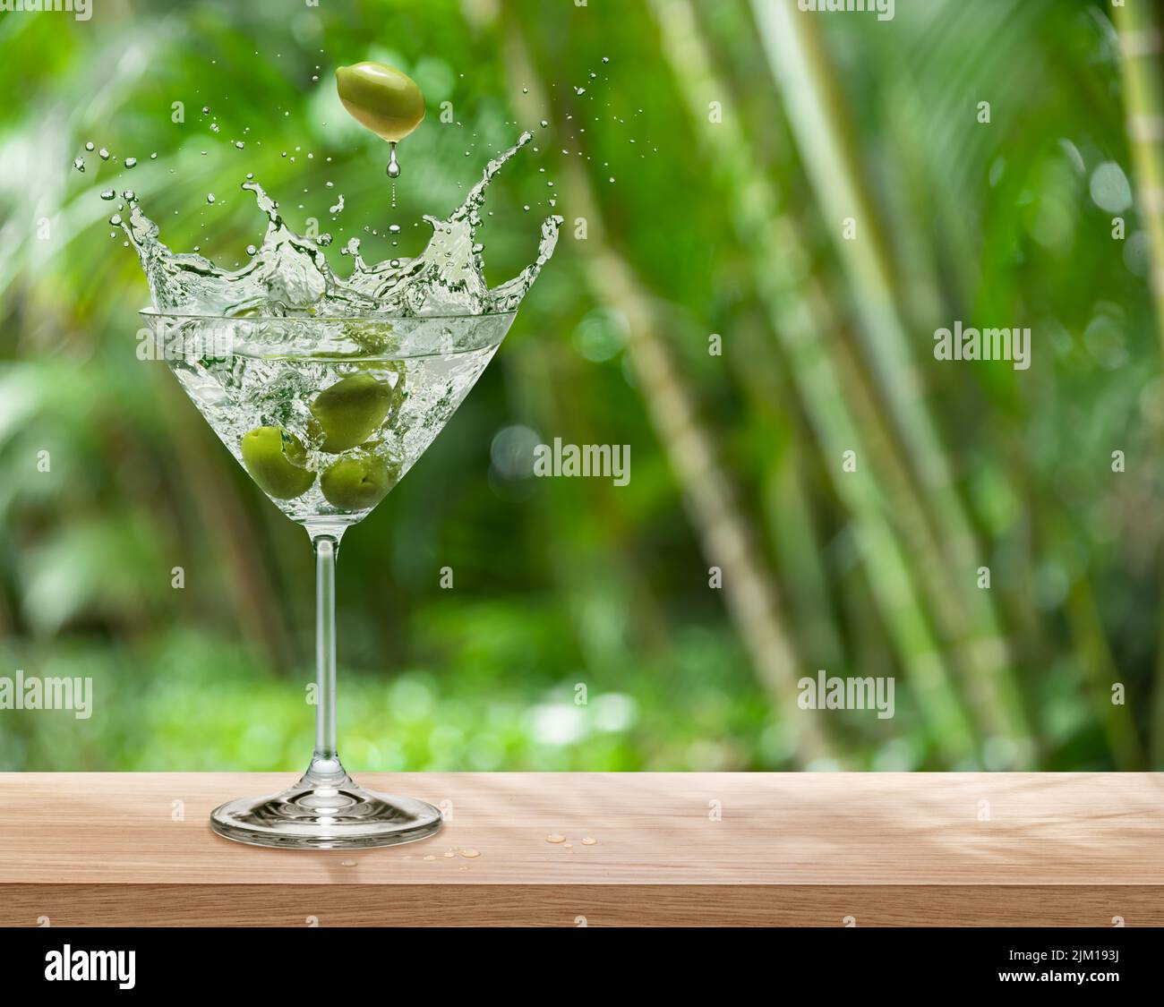 Martini glass with olives and beverage splash is on table top. Green