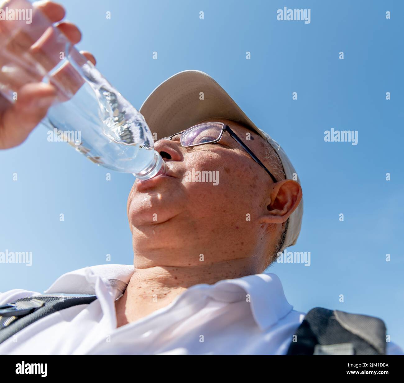 A senior man drinking plenty of water on a record breaking hot summer day to avoid dehydration while out and about. Stock Photo