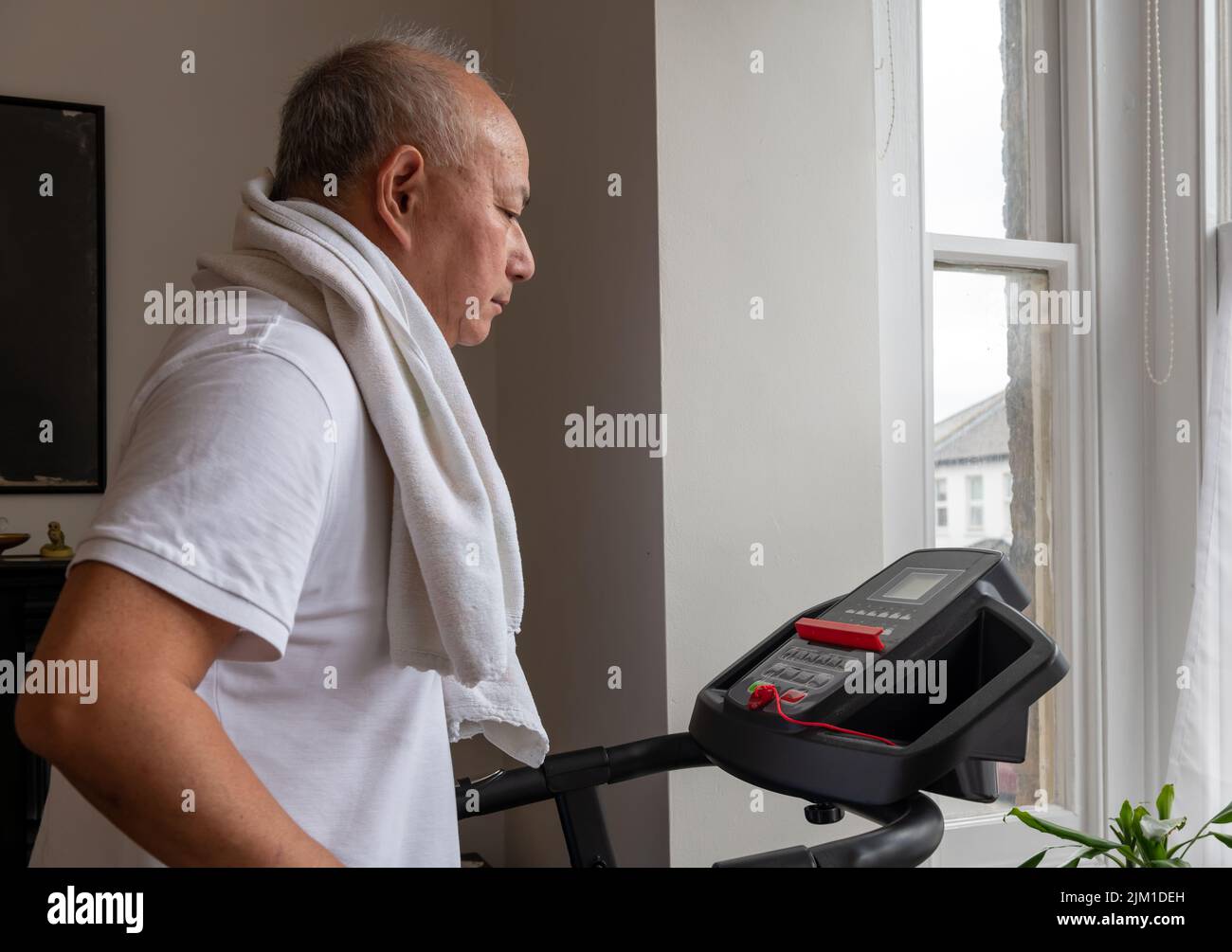 A senior man trying to keep fit working out on a treadmill at home. Stock Photo
