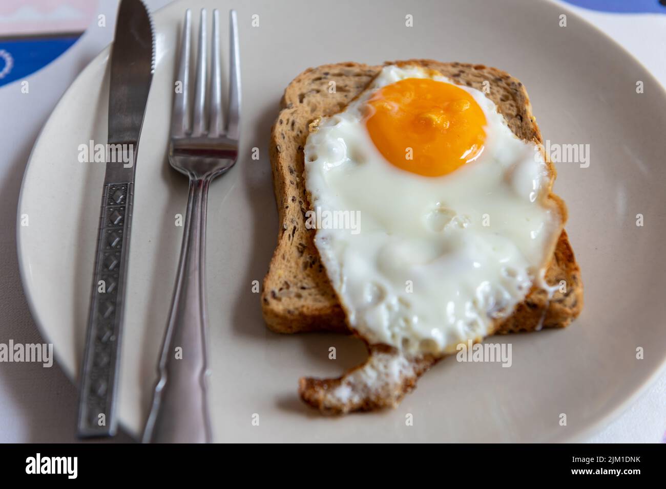 A fried egg on a slice of toasted bread on a plate with knife and fork. Stock Photo