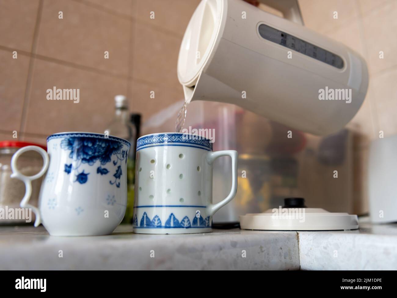 A person pouring boiled water to tea mugs. Energy use, cost of living concept. Stock Photo