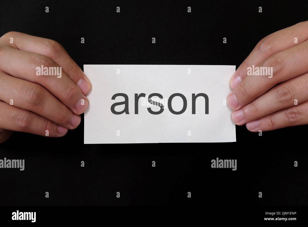 Arson crime case mug shot concept. Criminal hands holding paper placard with written word in dark black background. Stock Photo