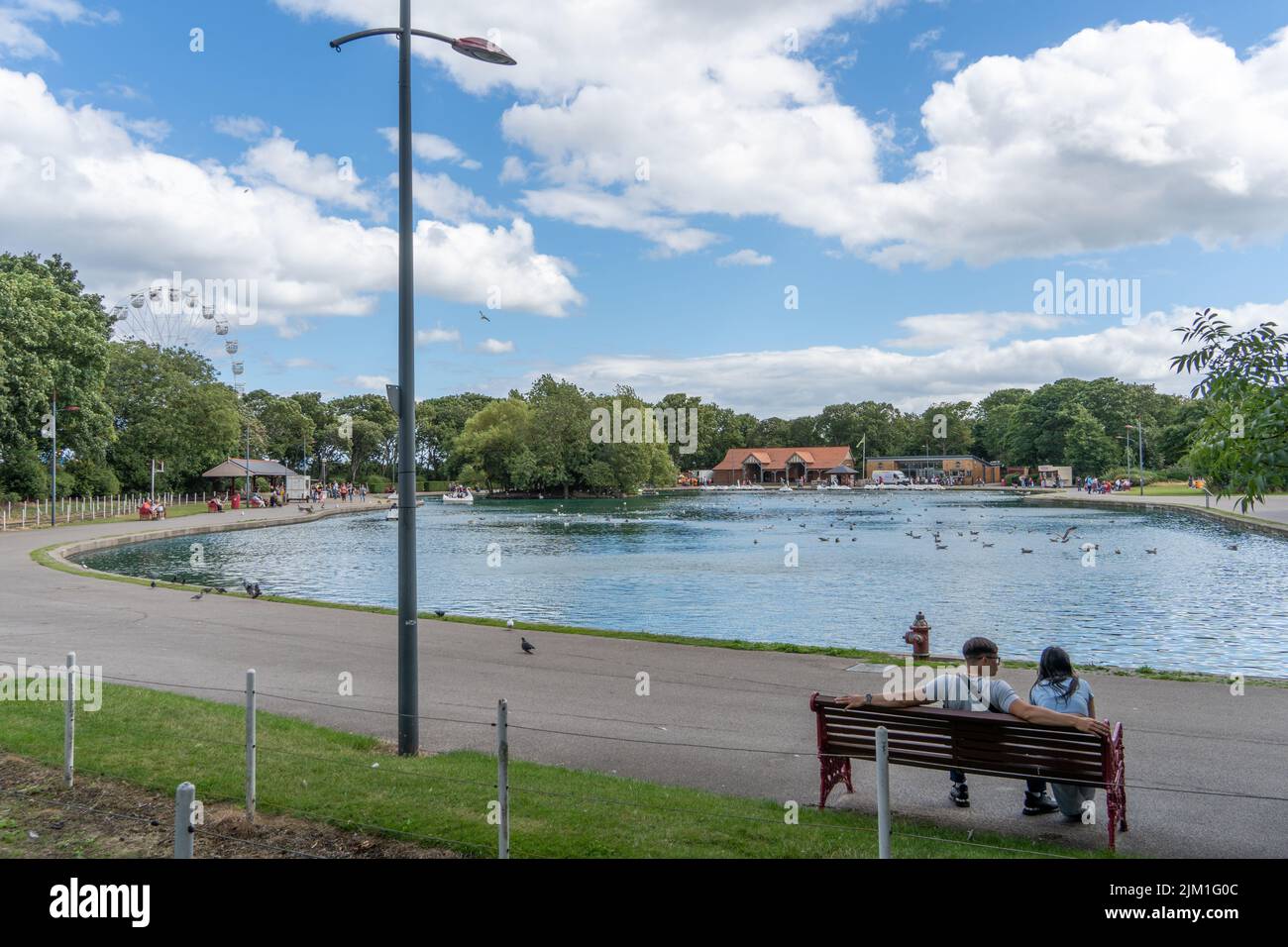 View of the lake at South Marine Park, South Shields, UK with a young couple sitting on a bench. Stock Photo
