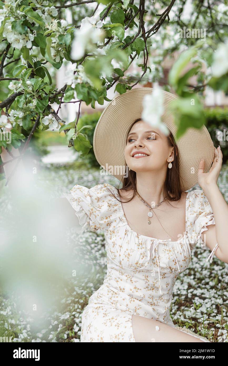 An attractive long-haired woman walks in the spring in the park of blooming apple trees. Stock Photo