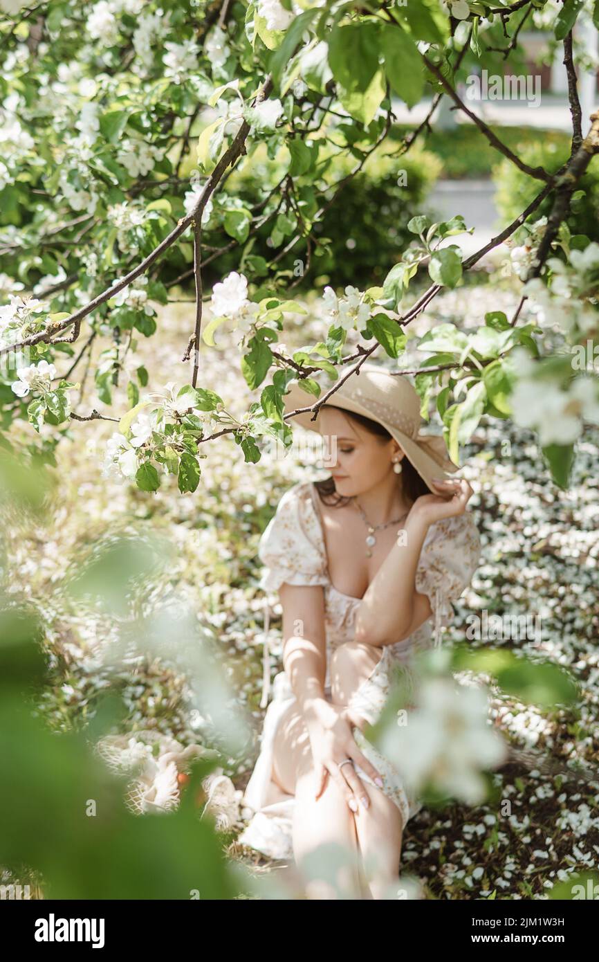 An attractive long-haired woman walks in the spring in the park of blooming apple trees. Stock Photo