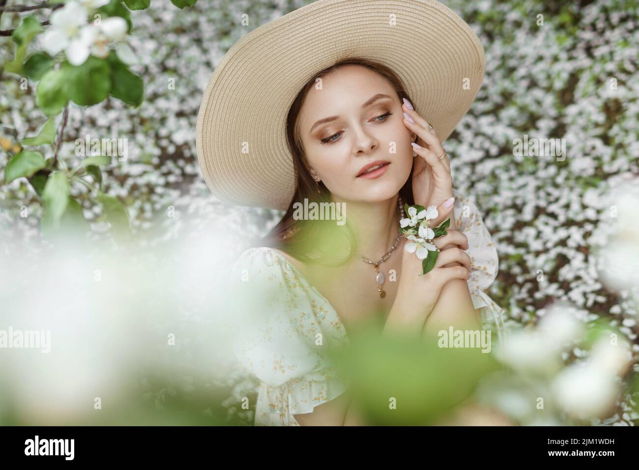 An attractive long-haired woman walks in the spring in the park of blooming apple trees. Stock Photo