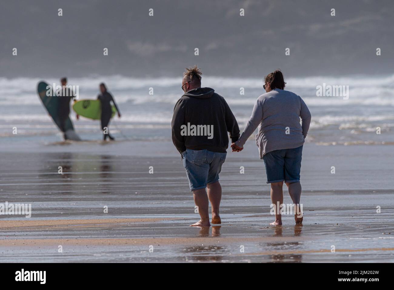 A couple walking and holding hands on Fistral Beach at low tide in Newquay in Cornwall in the UK. Stock Photo